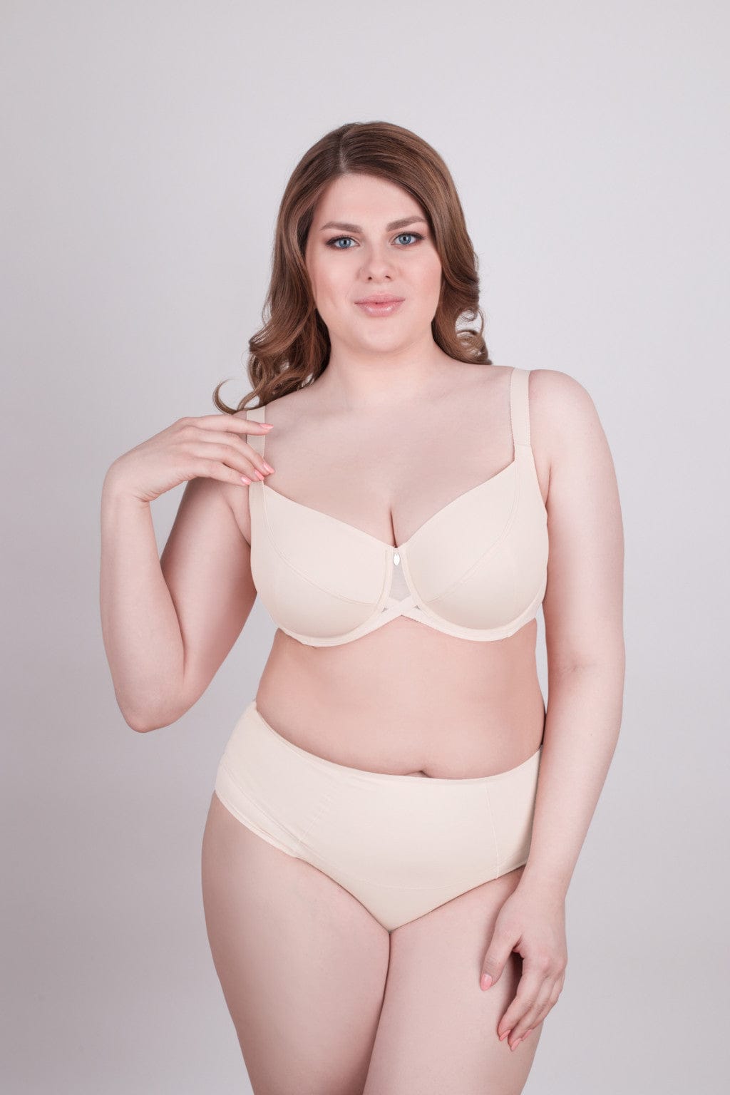 A beige underwire bra with a matching pair of high-waisted briefs worn by a woman against a plain light gray background.