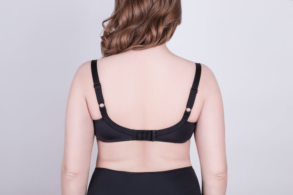 A black bra viewed from the back on a person, featuring adjustable shoulder straps and a hook-and-eye closure against a plain light gray background.