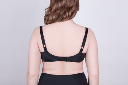 A black bra viewed from the back on a person, featuring adjustable shoulder straps and a hook-and-eye closure against a plain light gray background.