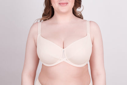 A beige full-coverage underwire bra with wide shoulder straps and a small decorative detail at the center gore worn by a person.