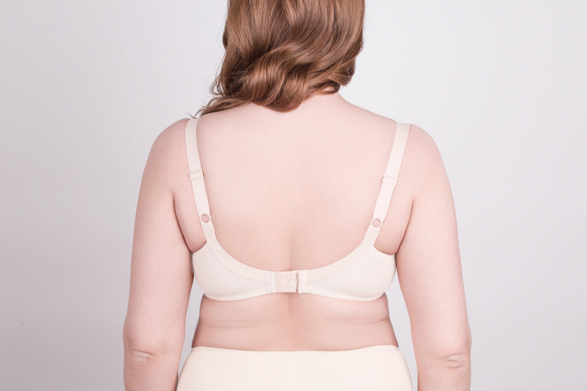 A beige bra shown from the back on a person with fair skin, featuring adjustable shoulder straps and a hook-and-eye closure.