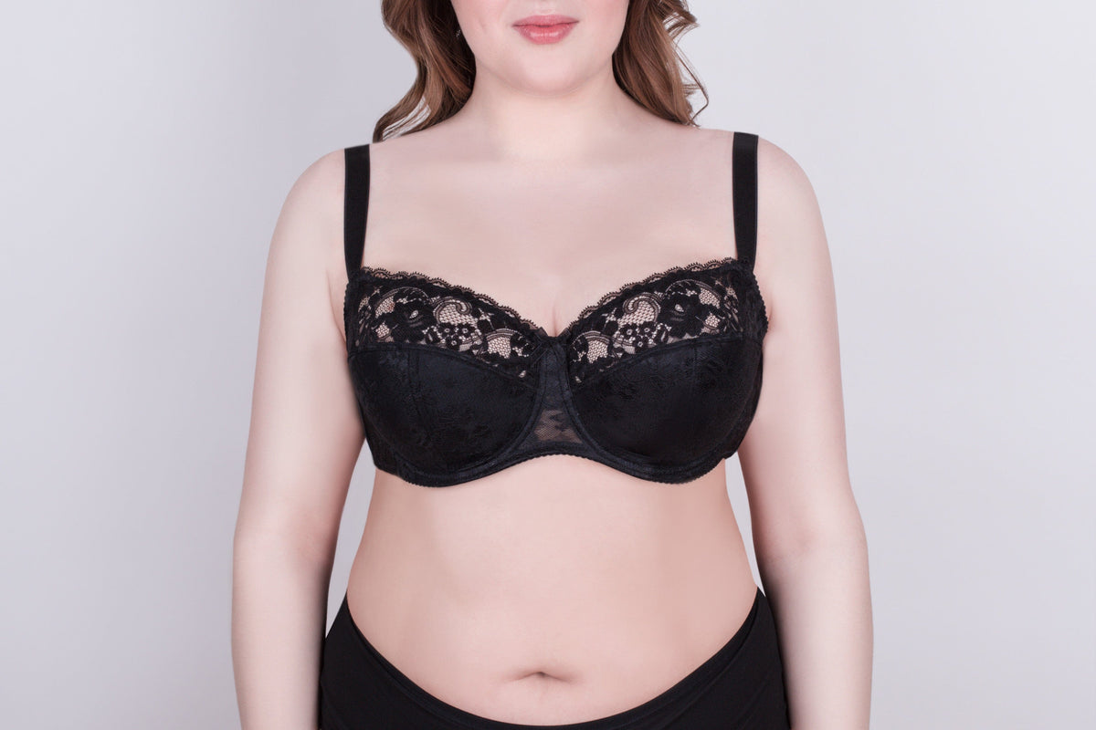 A black lace bra with adjustable straps worn by a person against a plain light gray background.