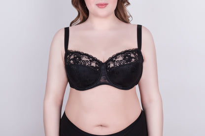 A black lace bra with adjustable straps worn by a person against a plain light gray background.