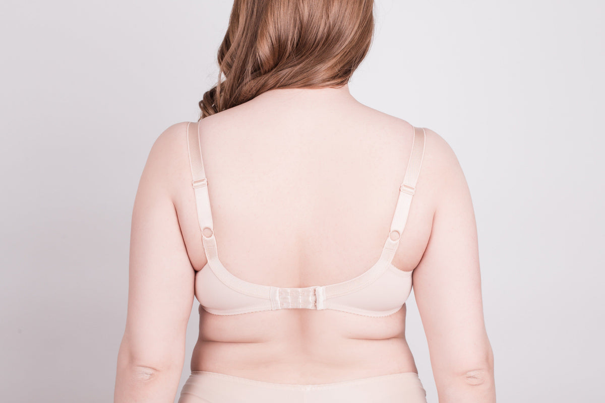 A beige bra viewed from the back on a woman with long light brown hair against a plain light gray background.