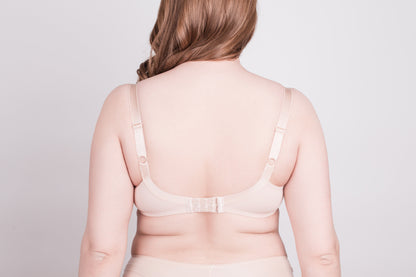 A beige bra viewed from the back on a woman with long light brown hair against a plain light gray background.