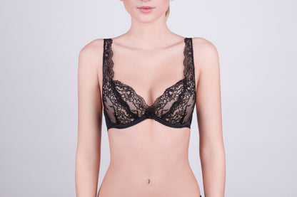 A black lace bra with wide lace-trimmed shoulder straps worn by a woman against a plain light gray background.