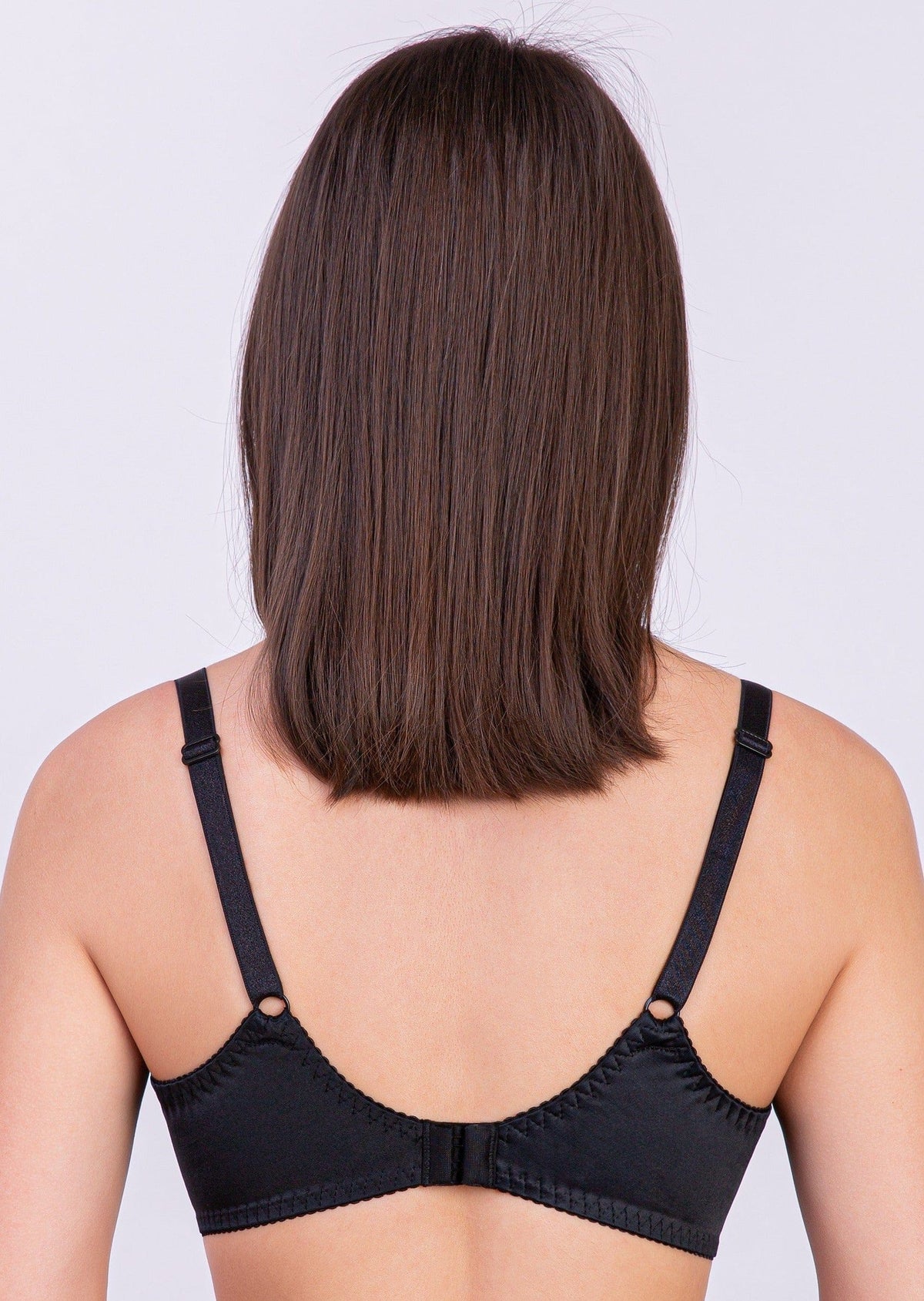 A person viewed from behind wears a black bra featuring adjustable shoulder straps with round metal connectors against a plain white background.