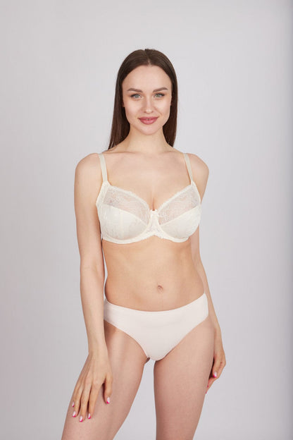 A woman wearing a beige lace-detailed balconette bra and matching plain bikini-style underwear against a light grey background.