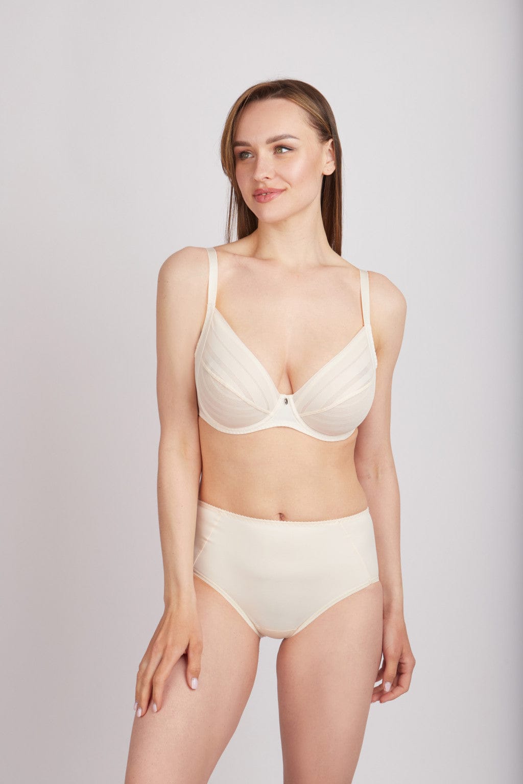 A model stands wearing a cream-colored bra with a paneled design and matching high-waisted briefs against a plain light gray background.