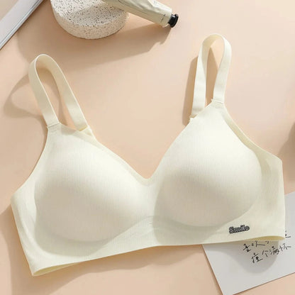 A beige ribbed wireless bra featuring adjustable straps and a small metal 'Smile' emblem on the lower right cup, displayed against a light background with a cream-colored tube and a paper card.