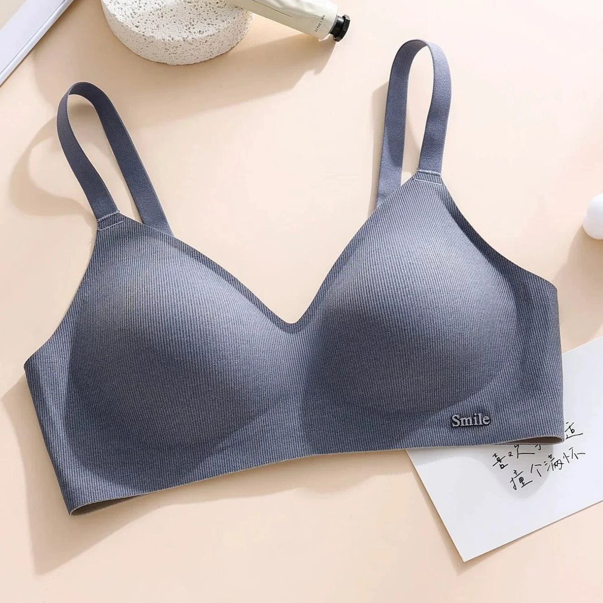 A seamless grey bralette featuring wide shoulder straps, a ribbed texture, and a small metal logo plaque reading Smile at the lower right edge.