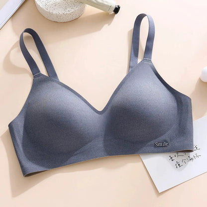 A seamless grey bralette featuring wide shoulder straps, a ribbed texture, and a small metal logo plaque reading Smile at the lower right edge.