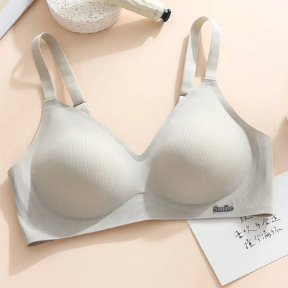 A light grey ribbed bralette with adjustable shoulder straps and a small decorative embroidery reading "Smile" on the bottom band sits on a light-colored surface next to a piece of paper.