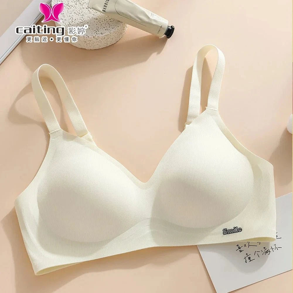 A beige ribbed wireless bra with wide shoulder straps and a small 'Smile' tag on the lower band, displayed on a neutral surface next to a tube of cream and a piece of paper.