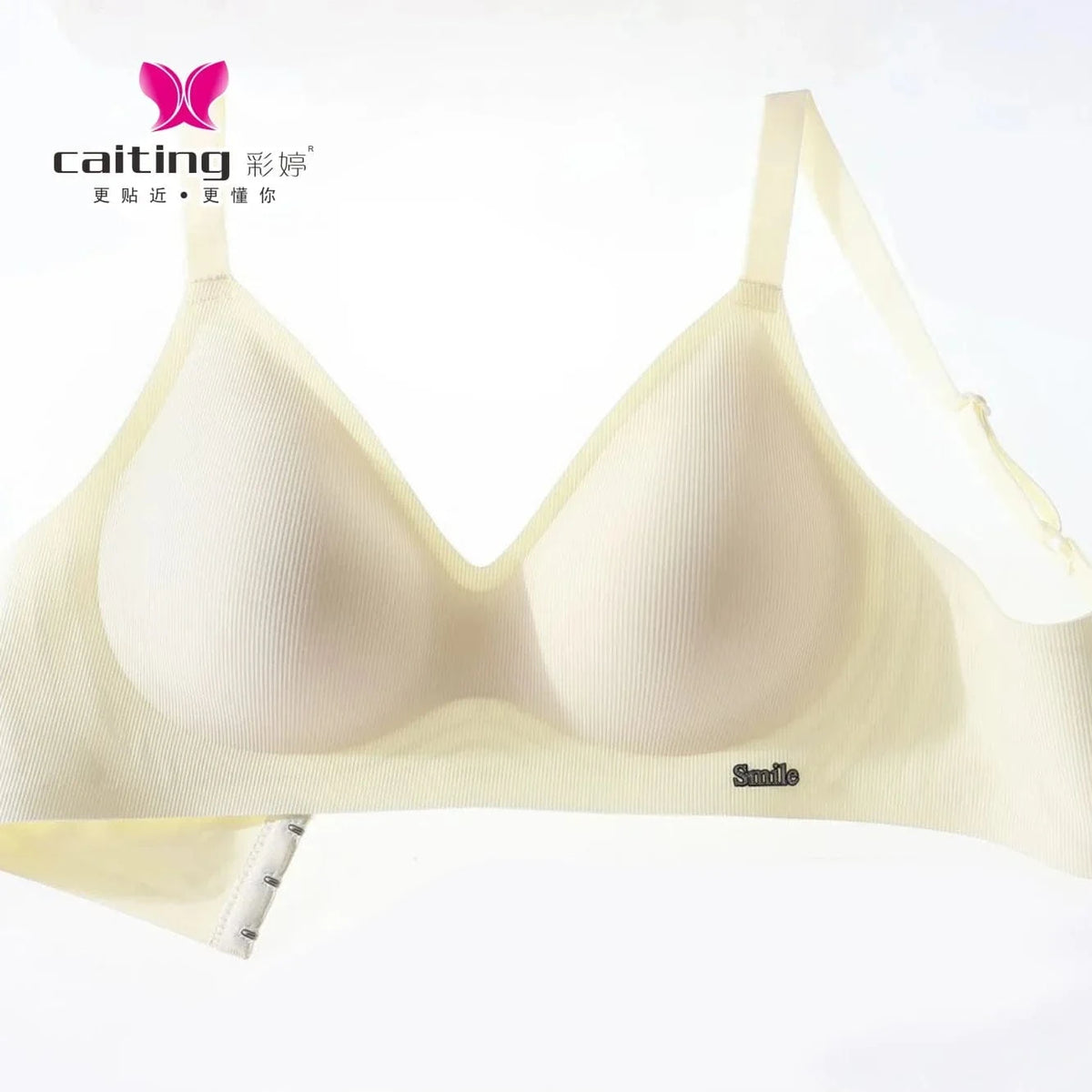 A beige wireless bra features ribbed fabric, thin adjustable shoulder straps, and a small metal "Smile" label on the lower front band against a white background.