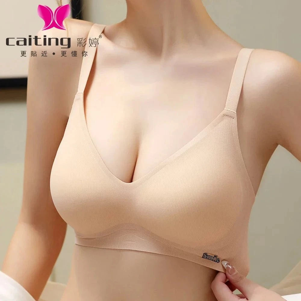 A beige wireless V-neck bra with ribbed texture and a small metallic logo detail on the side band, worn by a person.