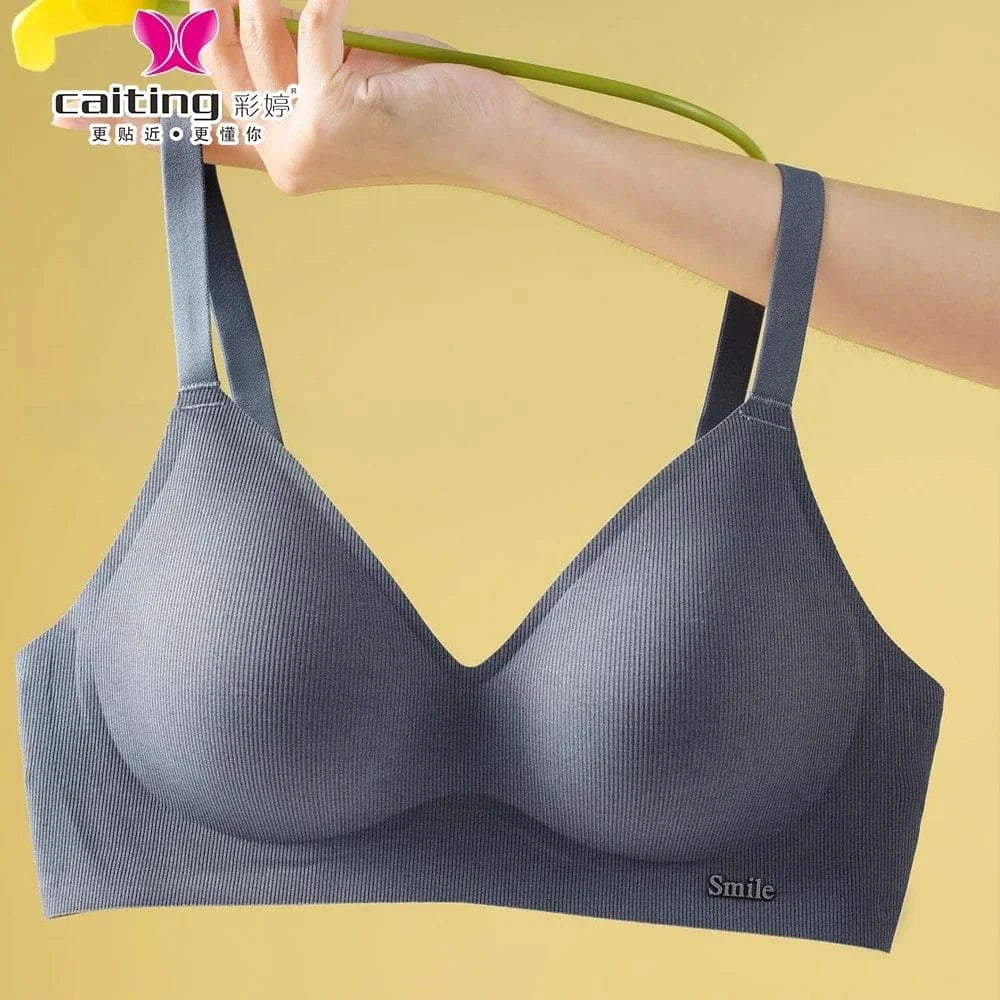 A grey seamless wireless bra with a ribbed texture and a small metal tag that reads Smile on the lower right side, held up by a hand against a yellow background.