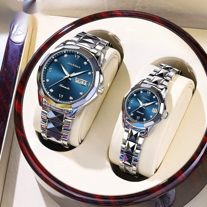 A pair of metallic watches with blue circular faces and decorative link bands sit inside an open round wooden display case.