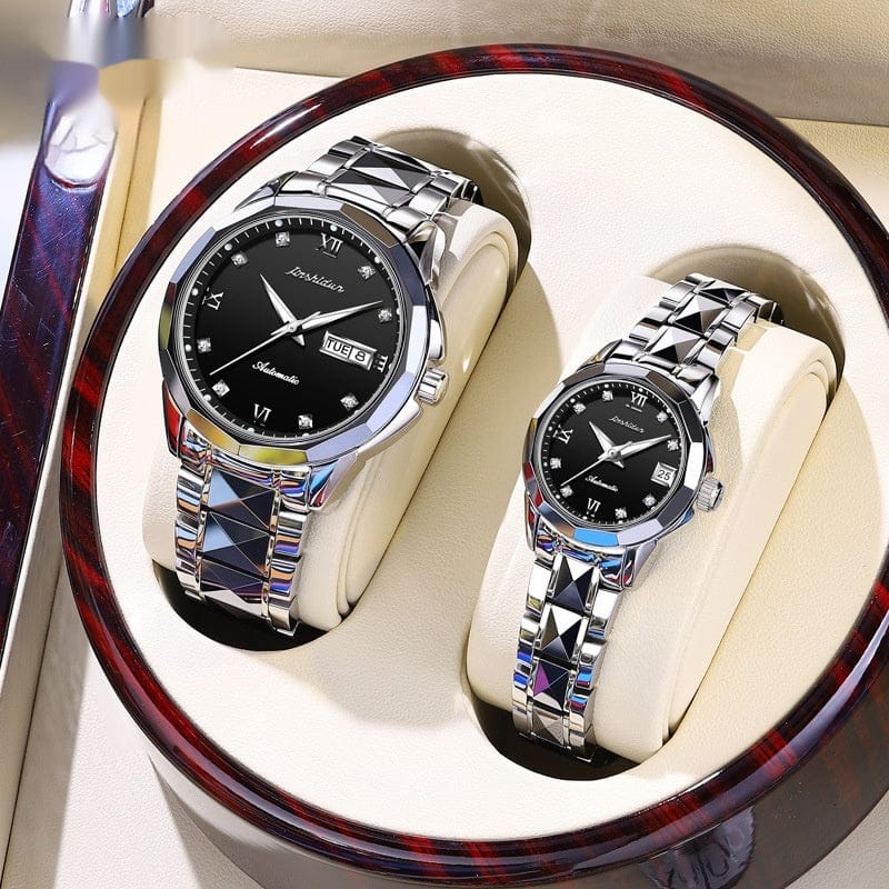 A pair of matching silver-tone automatic wristwatches with black dials, diamond-style hour markers, and unique geometric link bracelets displayed side-by-side inside a round wooden presentation box.