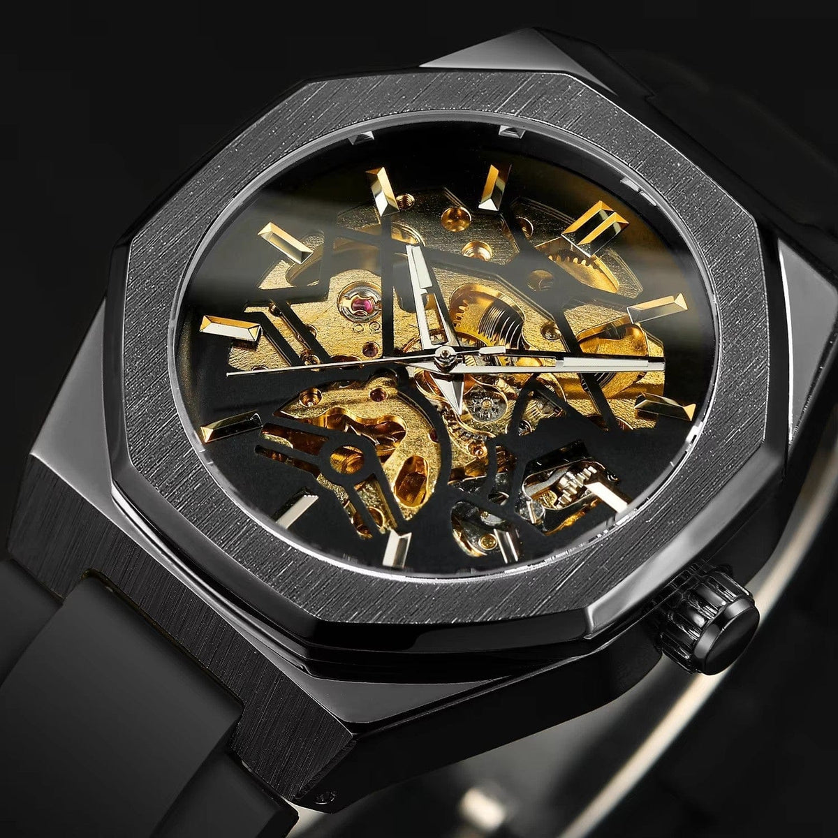 A skeleton watch featuring a black octagonal bezel and case with an exposed gold-tone mechanical movement and black silicone strap against a black background.