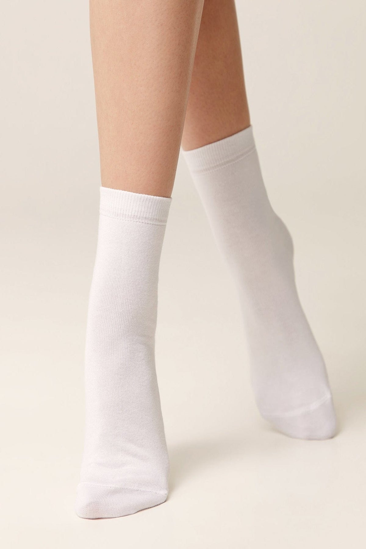 A pair of plain white crew-length socks worn on a person's feet against a neutral background.