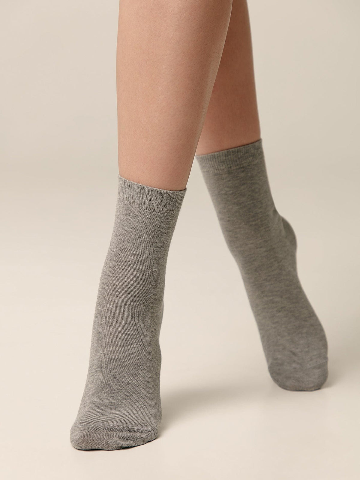 A pair of mid-calf grey socks worn on a person's legs against a solid light background.