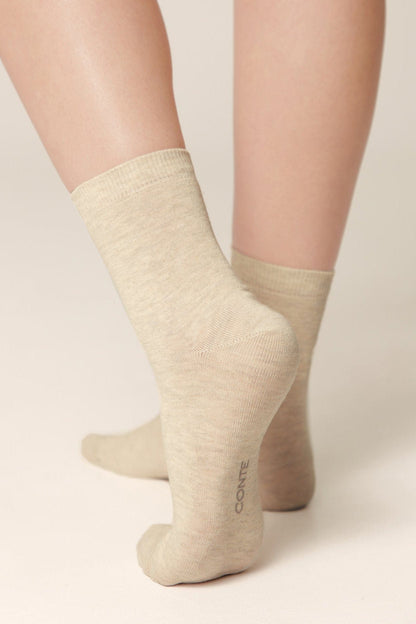 A pair of beige crew socks on a person's feet, viewed from behind against a plain neutral background.