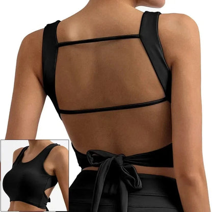 A black athletic crop top shown from the back, featuring two horizontal straps across the open back and a tie closure at the waist, with an inset showing the side view.