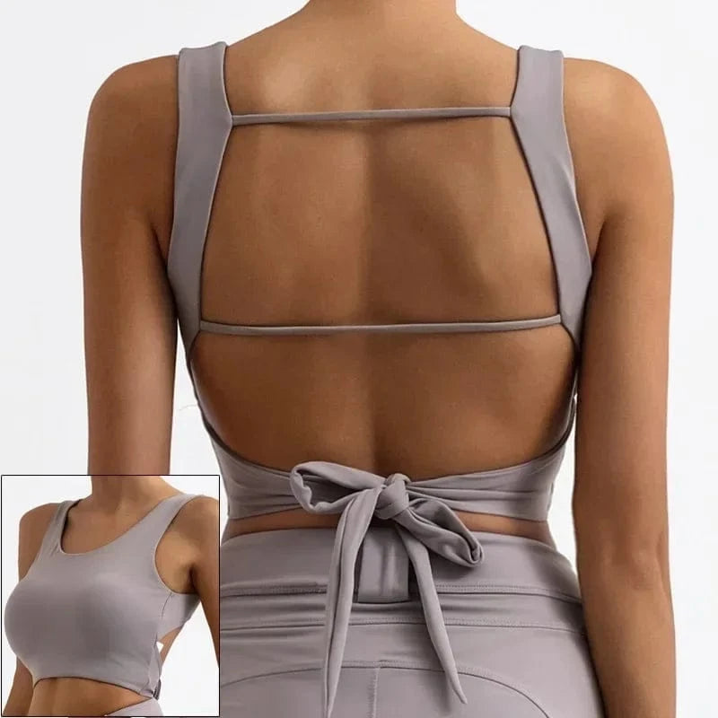 A lavender-grey athletic crop top with a wide open back, featuring two horizontal straps and a tie-closure at the lower back, shown from both the back and a side angle.