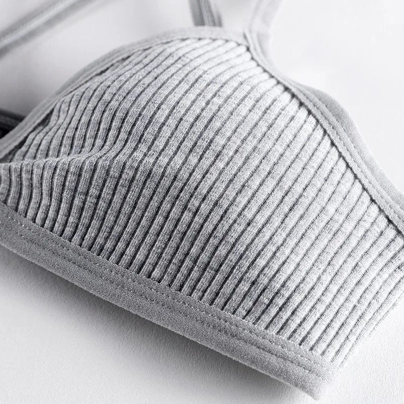 A close-up view of a grey ribbed fabric bralette featuring a wide stitched elastic hem and thin shoulder straps against a plain white background.