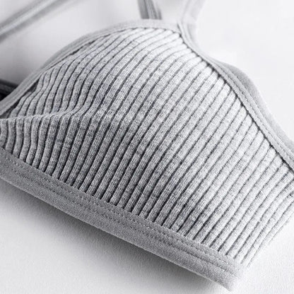 A close-up view of a grey ribbed fabric bralette featuring a wide stitched elastic hem and thin shoulder straps against a plain white background.