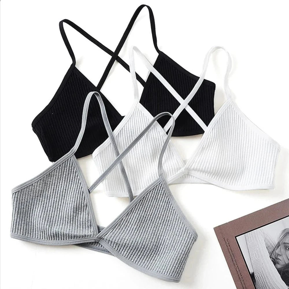 Three ribbed bralettes with crisscross strap detailing are arranged on a white surface, presented in black, white, and grey colorways.