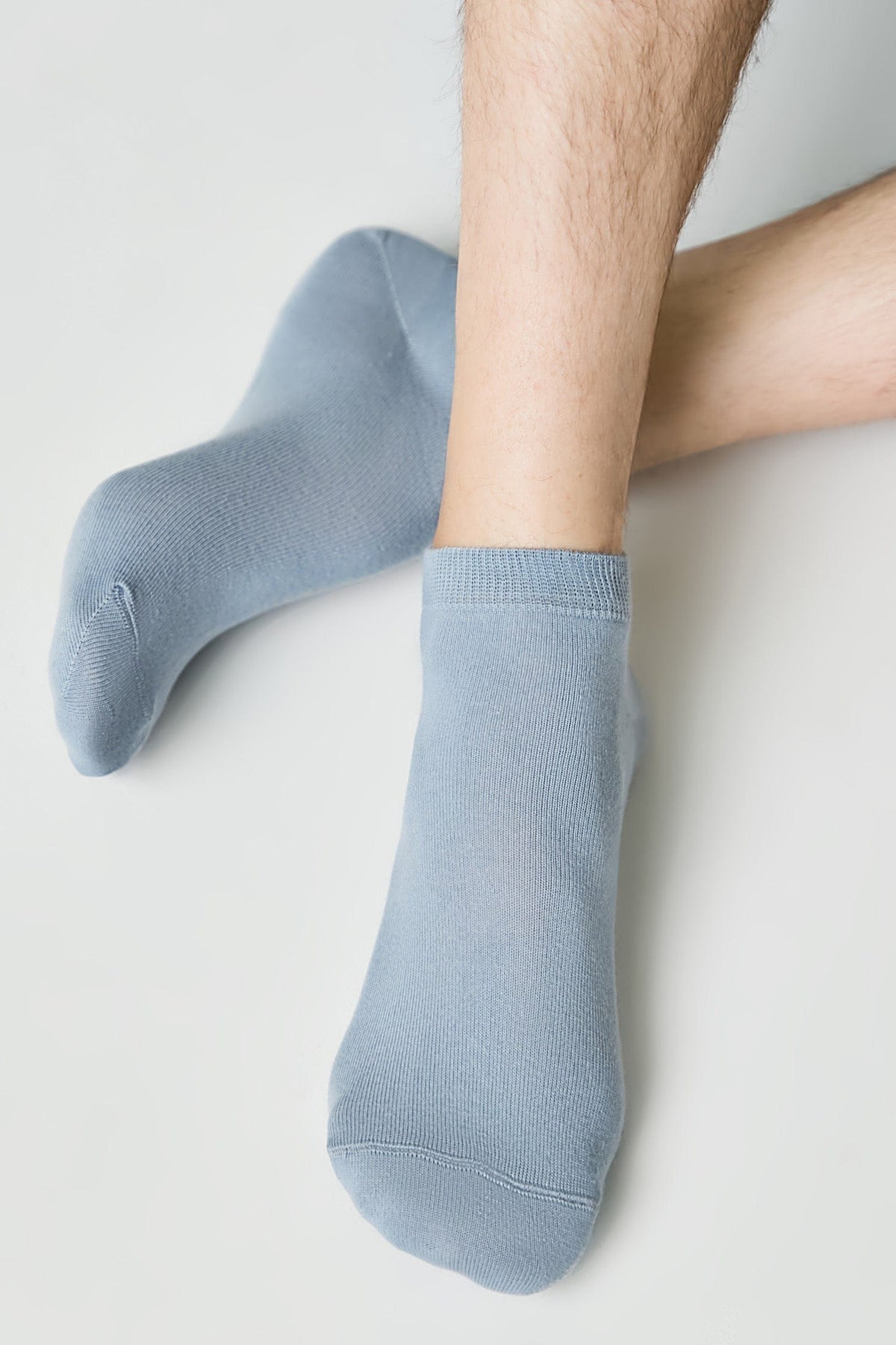 A pair of ankle socks in a soft blue shade are worn on a person's feet against a plain white background.