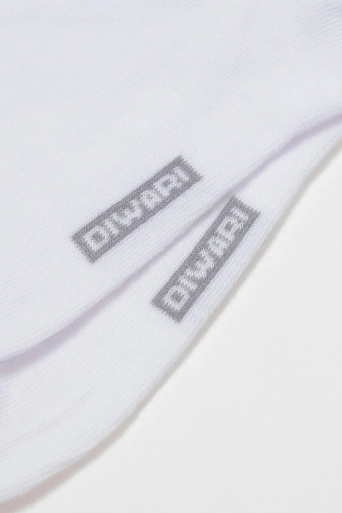 A close-up view of two white cotton socks, each featuring a small grey rectangular logo patch with the word DIWARI printed in a pixelated font.