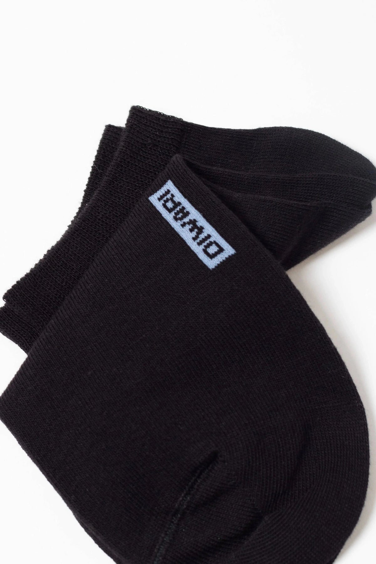 A pair of black ankle socks folded against a white background, featuring a light blue rectangular label with dark blue text on the top cuff.