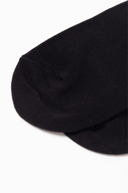 A close-up of the heel area of a plain black sock set against a white background.