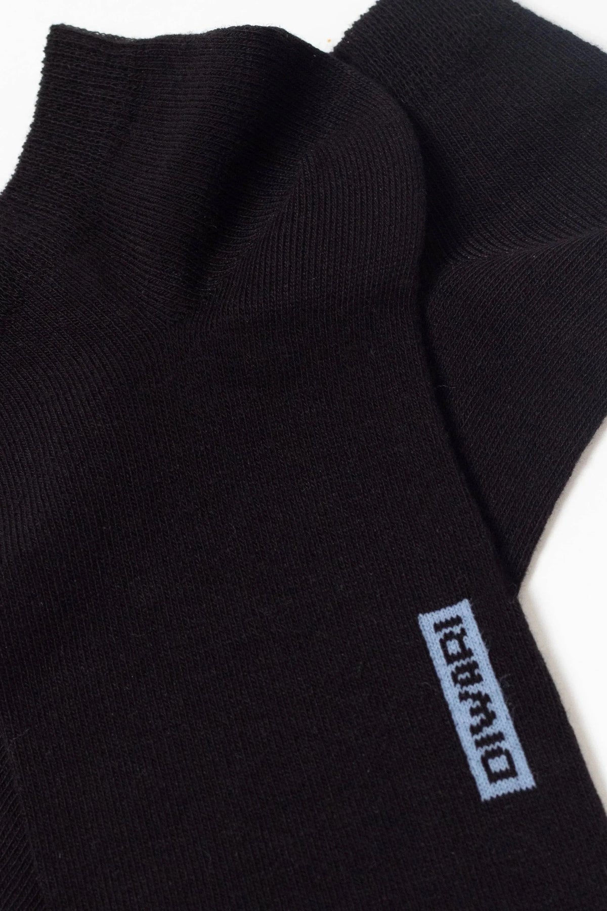 A pair of black ankle socks featuring a light blue rectangular logo with dark text near the cuff.