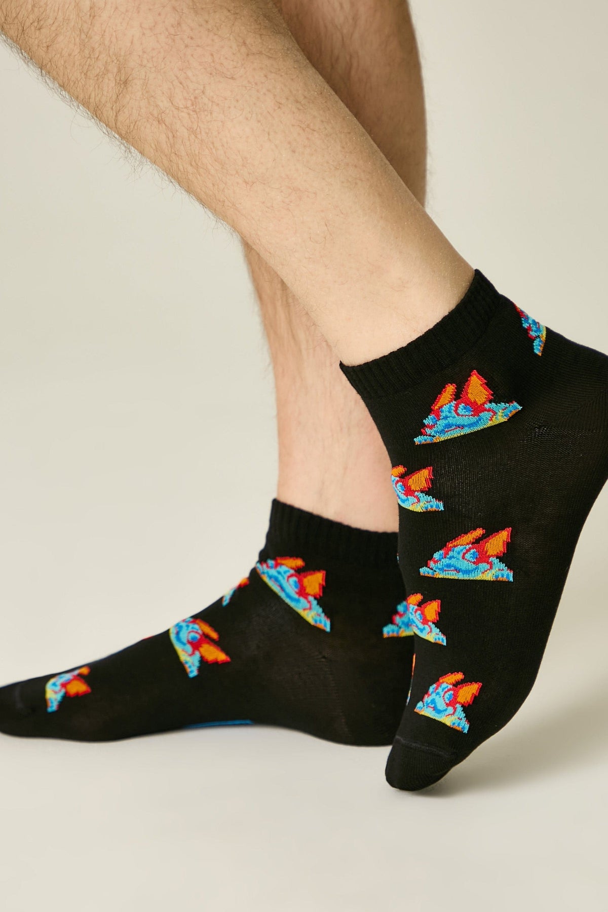 Black ankle socks patterned with small, colorful cartoon-style dragon motifs worn on a person's feet.