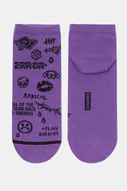 A pair of purple ankle socks feature a black graphic pattern on the left sock, including a skull, a sad face, the word RADICAL, and various small symbols, while the right sock is solid purple with a small black rectangular logo on the heel.