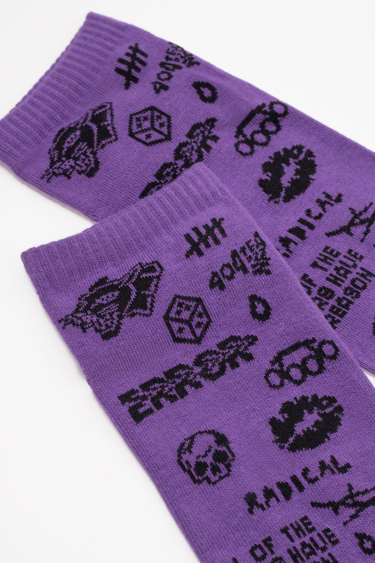 A pair of purple crew socks feature a repeating black pattern of symbols, including tally marks, a die, a skull, a lip print, and the words ERROR and RADICAL.