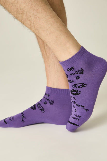 A pair of purple ankle socks worn on a person's feet, featuring a scattered black pattern of hand-drawn sketches, symbols, and text including the phrase 404 TEA.