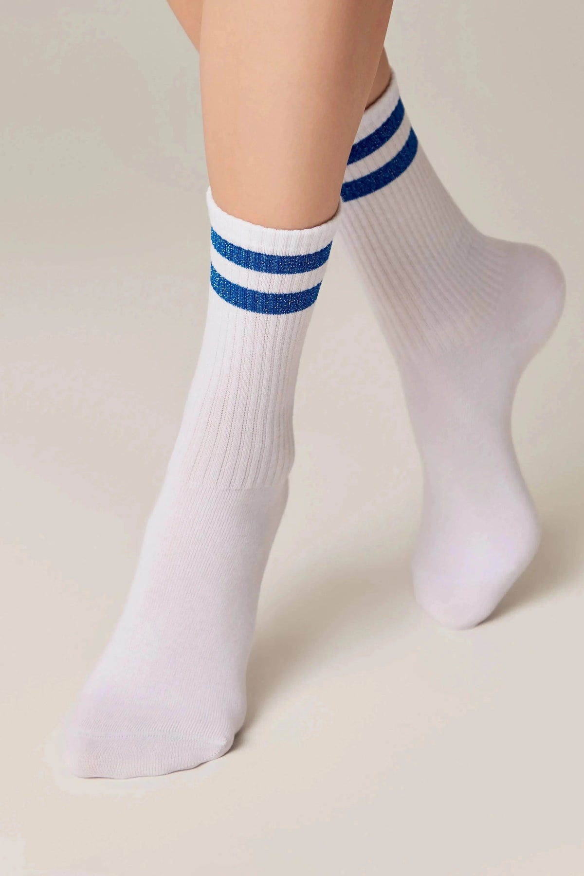 White crew socks with two horizontal blue glitter stripes at the ribbed cuffs, worn on the feet and lower legs against a solid light background.