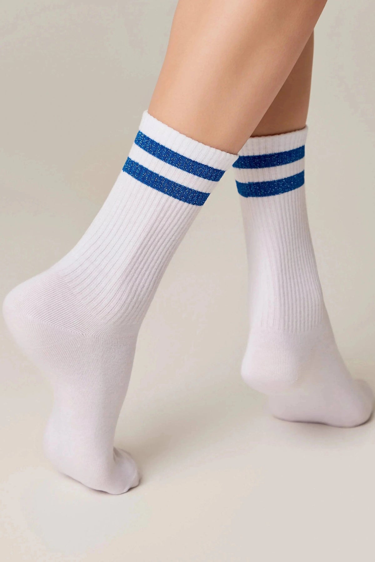 White ribbed crew socks feature two horizontal blue glitter stripes at the top, worn on a person's feet against a light background.