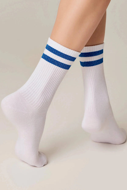 White ribbed crew socks feature two horizontal blue glitter stripes at the top, worn on a person's feet against a light background.