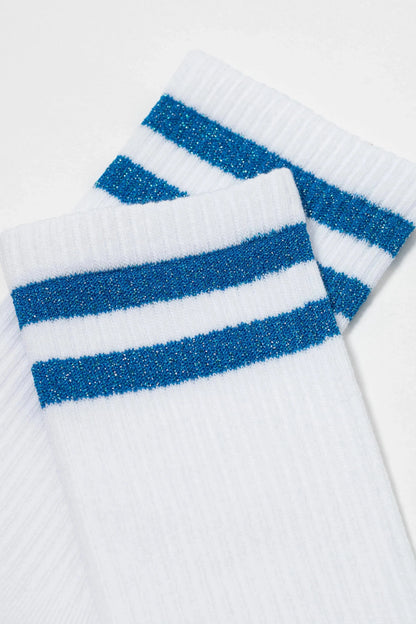A pair of white crew-length socks featuring two horizontal metallic blue glitter stripes near the ribbed cuffs.