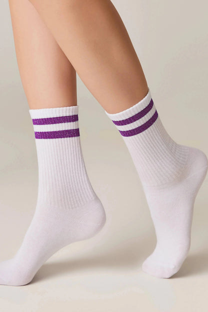 A pair of white crew-length socks featuring two horizontal glittery purple stripes around the upper ankle worn on a person's feet.