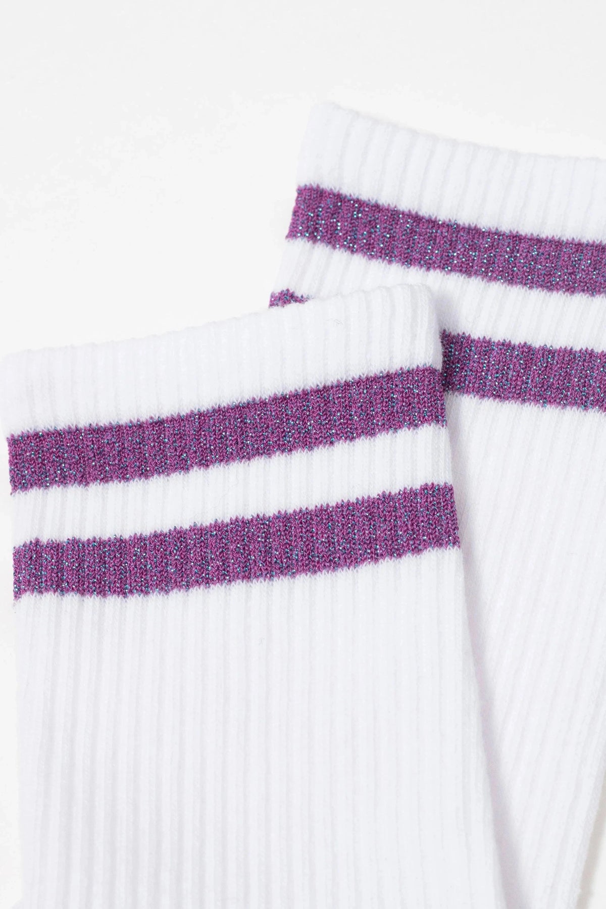 A pair of white ribbed crew socks featuring two horizontal purple glittery stripes on the cuffs.