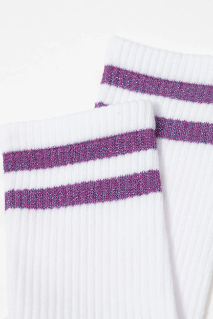 A pair of white ribbed crew socks featuring two horizontal purple glittery stripes on the cuffs.