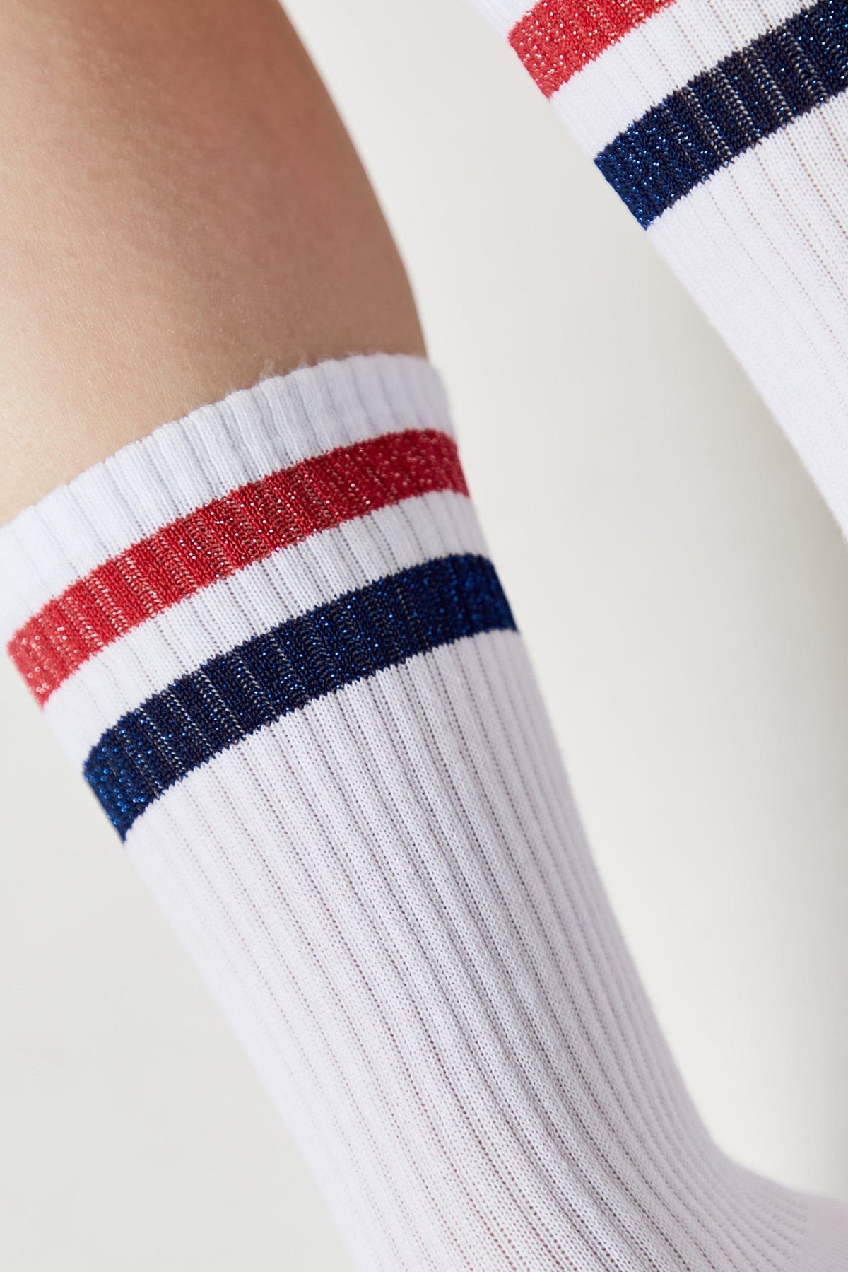 A close-up of a white ribbed athletic sock featuring two horizontal stripes in red and navy blue near the top cuff.