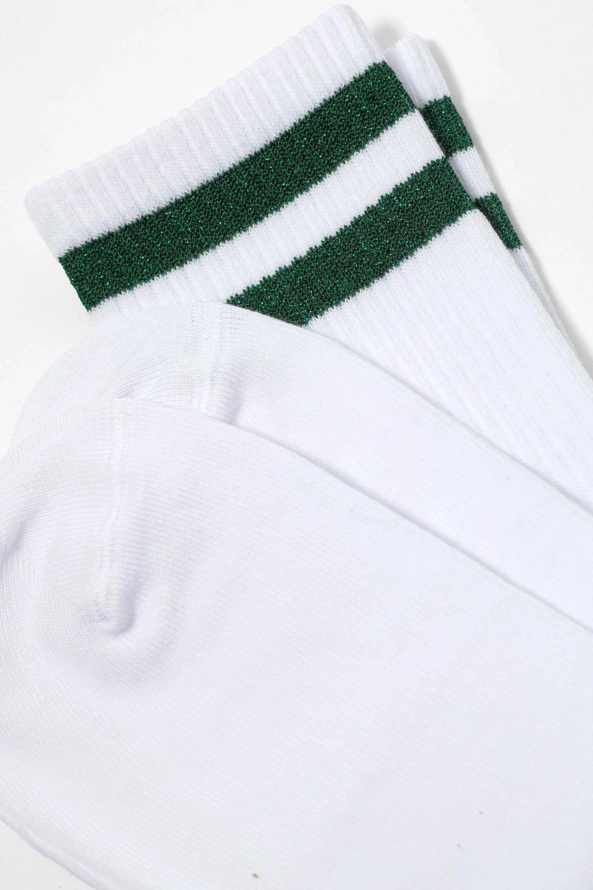 A pair of white mid-calf socks with two horizontal, glittering dark green stripes around the ribbed cuff.